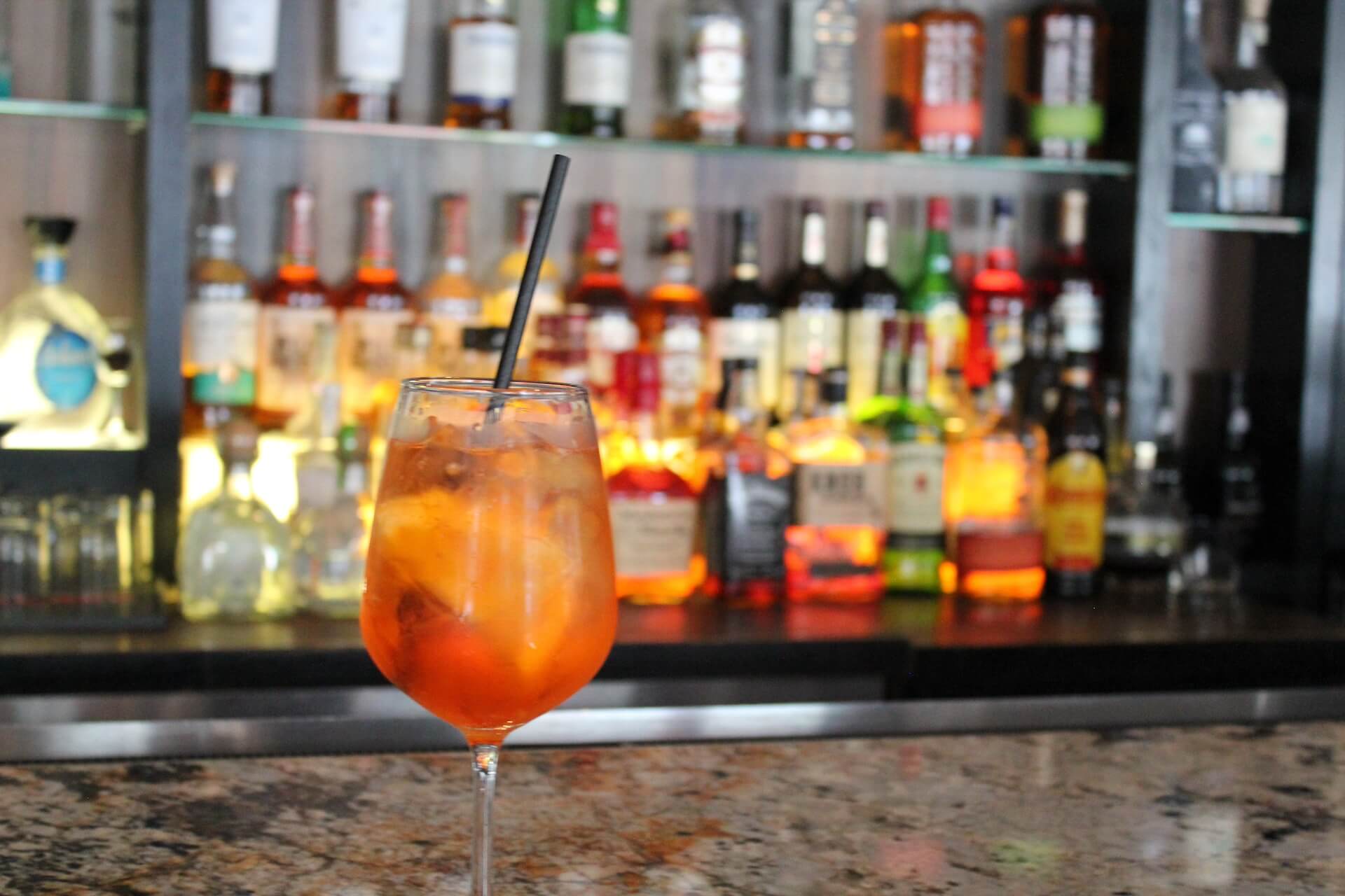 An orange spritz in a wine glass in front of the bar's rows of bottles