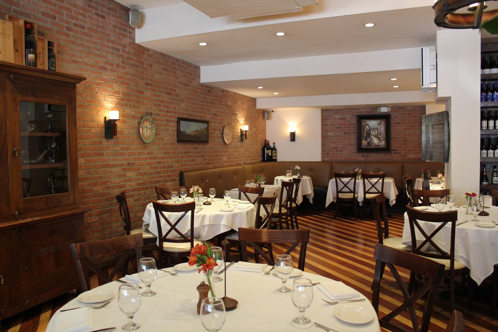 The dining room: a brick wall, round tables set with white linens and a wooden cabinet